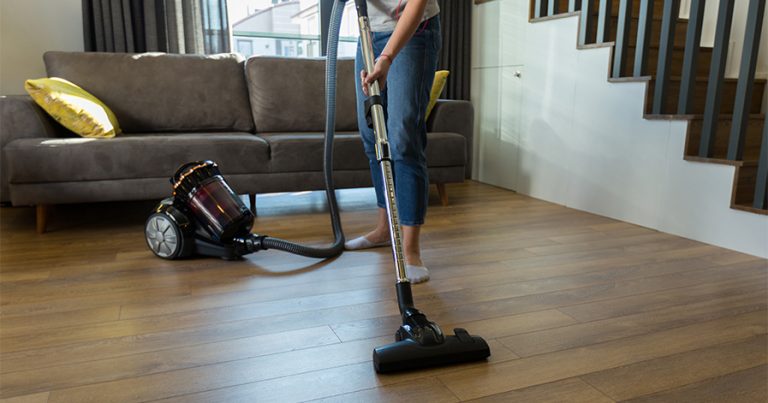 Woman vacuuming hardwood floor in living room area